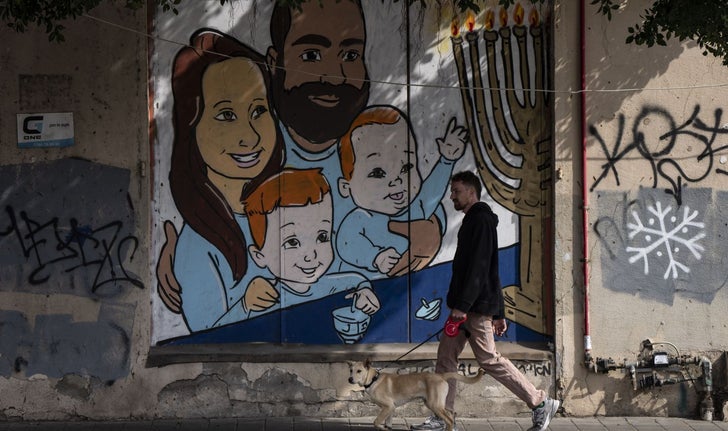 Un homme promenant son chien devant un graffiti représentant Shiri et Yarden Bibas, ainsi que leurs fils, Ariel, à gauche, et Kfir, à droite, qui ont été capturés par le Hamas. Seul le père, libéré le 1er février, est encore vivant.